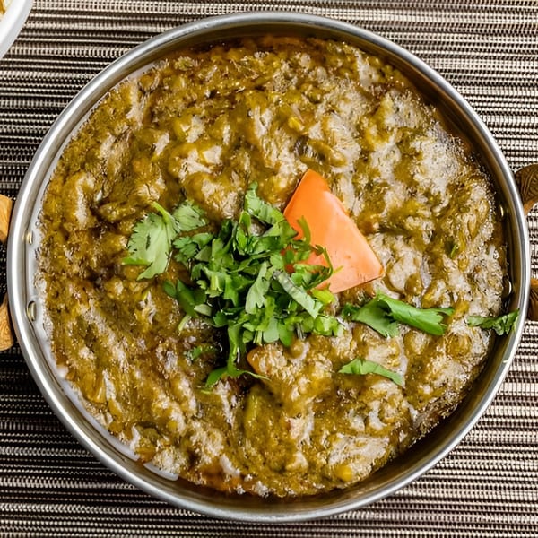 A metal bowl of green curry with cilantro and a carrot slice, served with white rice.